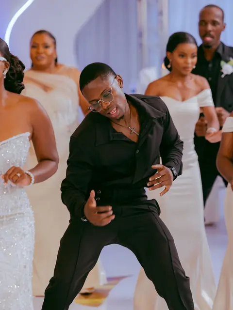 A groomsman dancing on a white floor surrounded by bridesmaids