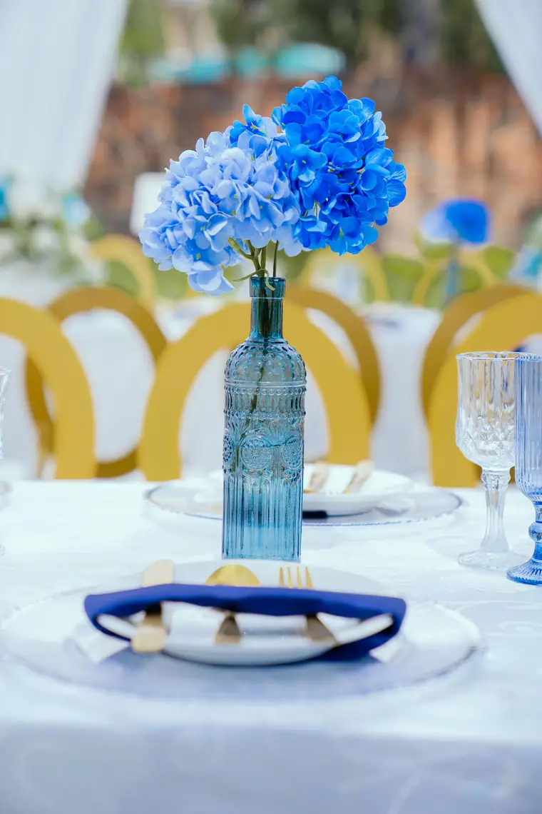 Blue hydrangeas in a glass bottle on a white and gold table