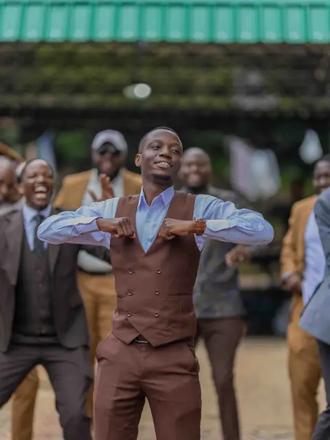 A groom in a brown suit dancing with his crowd