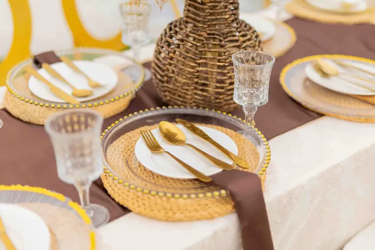 A table set with gold chargers, woven vase and brown napkins