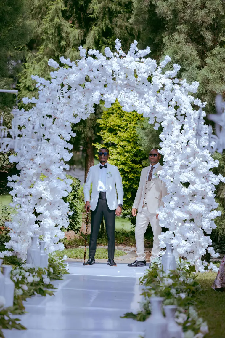 A groom and his best man waiting under a white flower arch