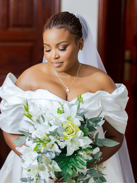 A bride in an off-shoulder gown looking down at her bouquet