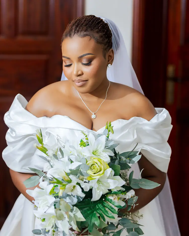 A bride in an off-shoulder gown looking down at her bouquet