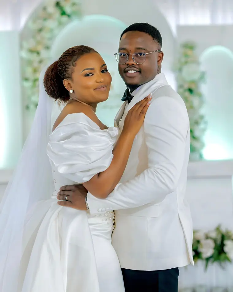 A smiling couple in white embracing in a floral hall