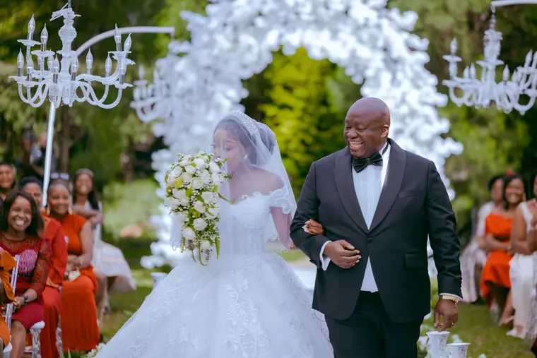 A father walks his daughter down a flower arch aisle