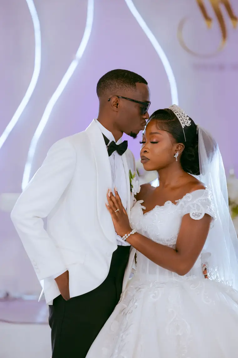 A groom kisses his bride's forehead in a white tuxedo